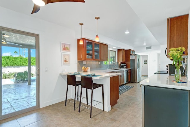 kitchen featuring pendant lighting, a breakfast bar area, appliances with stainless steel finishes, backsplash, and kitchen peninsula