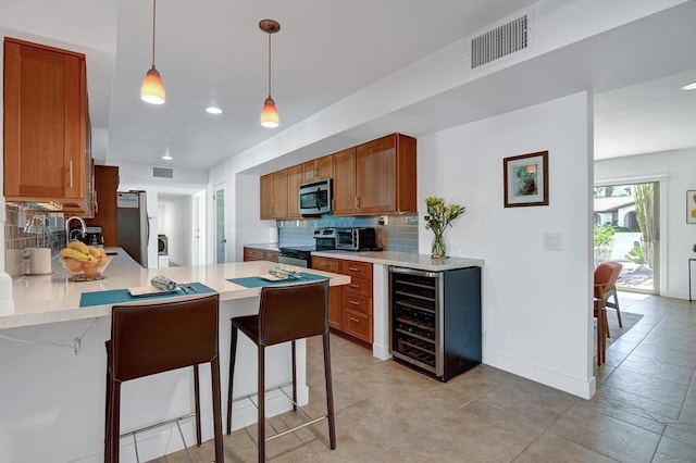 kitchen featuring hanging light fixtures, appliances with stainless steel finishes, a breakfast bar, and beverage cooler