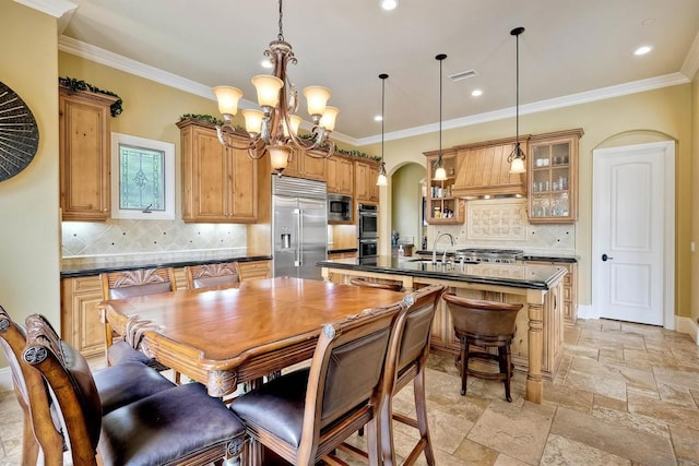 kitchen featuring built in appliances, an island with sink, decorative backsplash, hanging light fixtures, and a chandelier