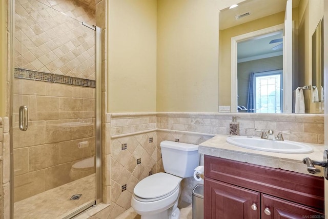 bathroom with toilet, walk in shower, crown molding, vanity, and tile walls