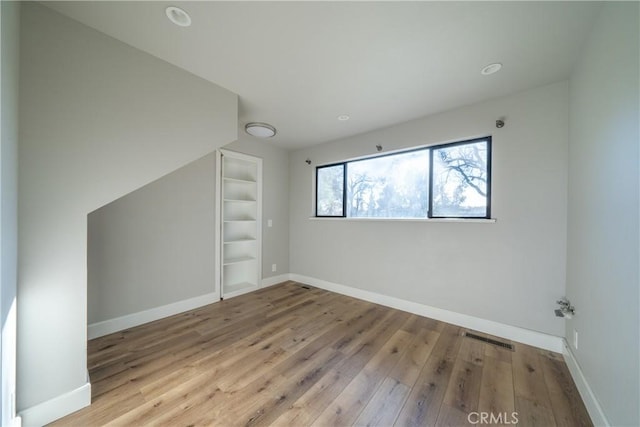 bonus room with light hardwood / wood-style floors and built in shelves