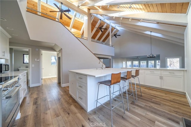 kitchen featuring white cabinets, decorative light fixtures, a kitchen island with sink, high end stainless steel range oven, and light hardwood / wood-style flooring