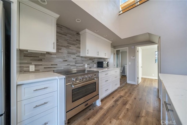 kitchen featuring tasteful backsplash, white cabinetry, light wood-type flooring, appliances with stainless steel finishes, and light stone counters