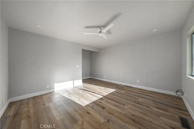 unfurnished room with a ceiling fan, wood finished floors, visible vents, and baseboards