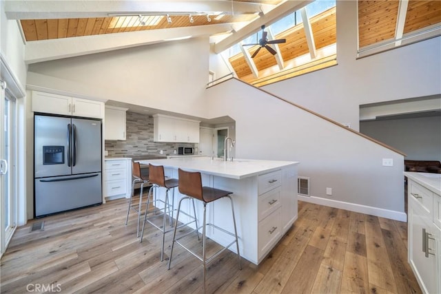 kitchen with white cabinetry, stainless steel appliances, vaulted ceiling with beams, backsplash, and a kitchen island with sink