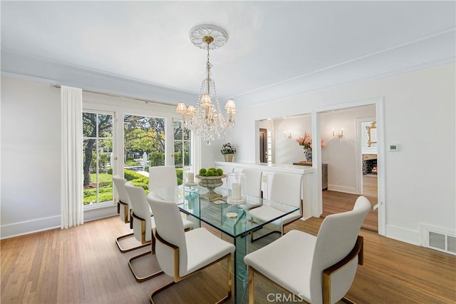 dining space with light hardwood / wood-style flooring, crown molding, and a chandelier