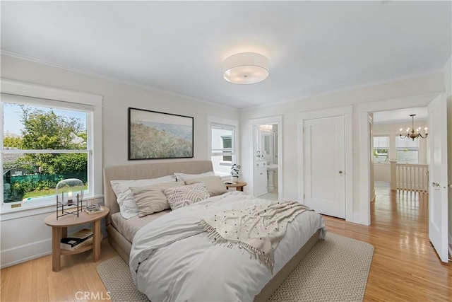 bedroom with connected bathroom, crown molding, an inviting chandelier, and light wood-type flooring