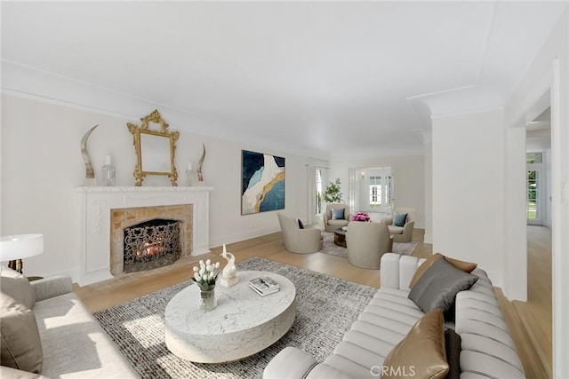 living room featuring light wood-type flooring, crown molding, and a tiled fireplace