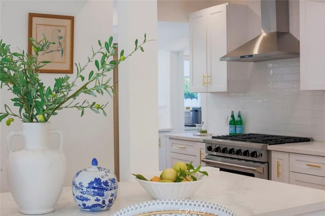 kitchen with tasteful backsplash, wall chimney exhaust hood, white cabinetry, and high end stainless steel range oven