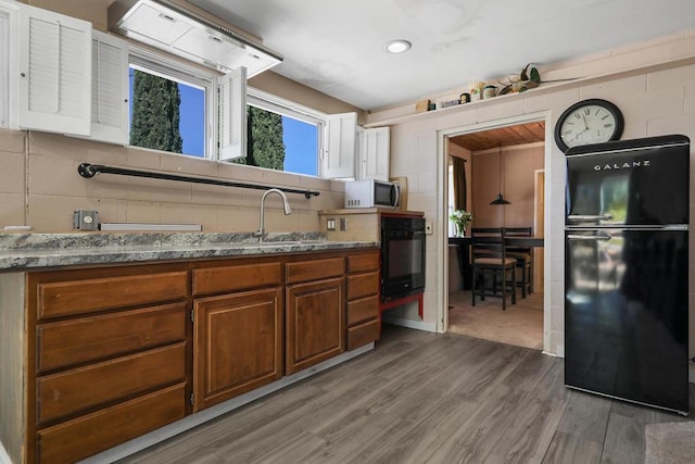 kitchen with sink, hardwood / wood-style flooring, black appliances, and stone countertops