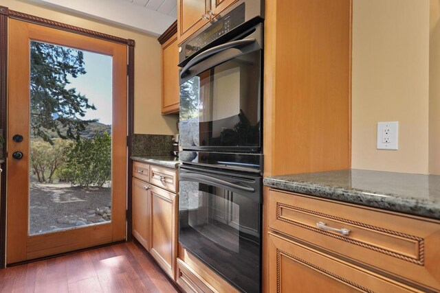 kitchen with dark stone countertops, dark wood-type flooring, a wealth of natural light, and double oven