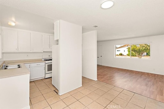 kitchen with a textured ceiling, white cabinetry, sink, light tile patterned floors, and stove