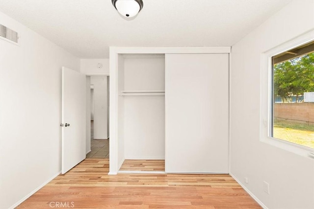 unfurnished bedroom featuring multiple windows, a closet, and light wood-type flooring