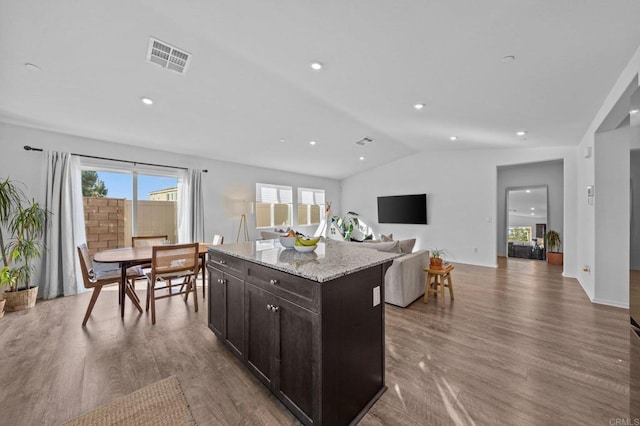 kitchen with light stone counters, hardwood / wood-style flooring, dark brown cabinets, and a kitchen island