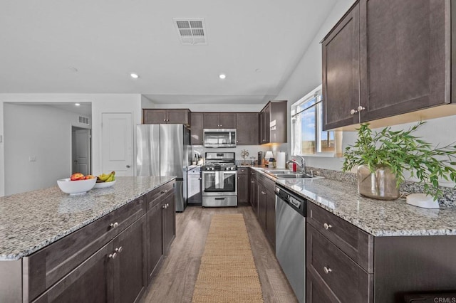 kitchen with appliances with stainless steel finishes, sink, a kitchen island, light hardwood / wood-style flooring, and light stone counters