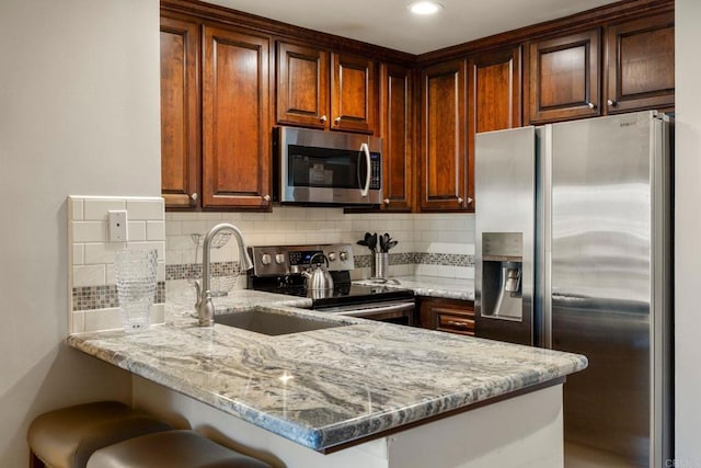 kitchen with light stone counters, appliances with stainless steel finishes, kitchen peninsula, and a breakfast bar