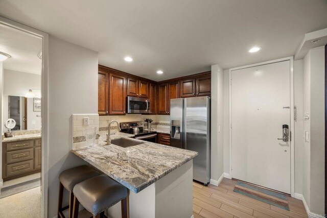 kitchen with kitchen peninsula, sink, light hardwood / wood-style flooring, stainless steel appliances, and light stone counters