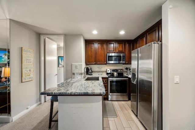 kitchen with kitchen peninsula, sink, light stone countertops, appliances with stainless steel finishes, and a breakfast bar area