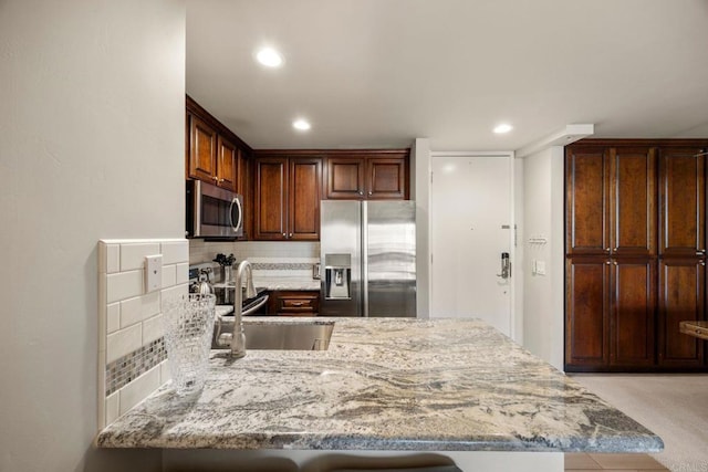 kitchen featuring backsplash, kitchen peninsula, sink, appliances with stainless steel finishes, and light stone counters