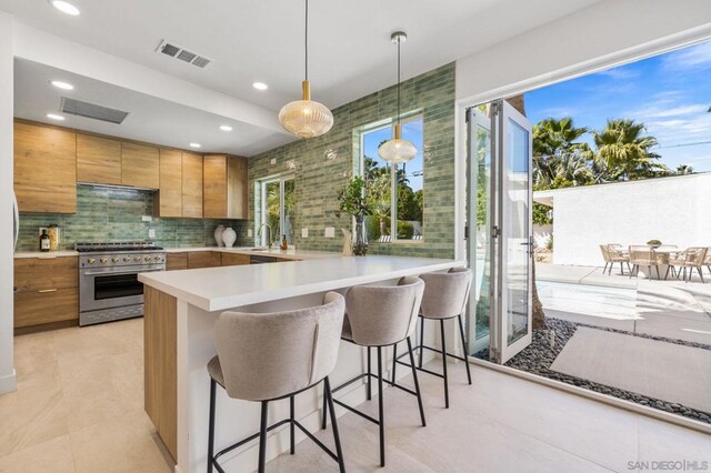 kitchen with stainless steel range, a kitchen breakfast bar, backsplash, hanging light fixtures, and kitchen peninsula