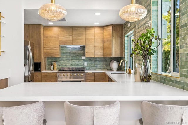 kitchen with decorative light fixtures, backsplash, kitchen peninsula, sink, and stainless steel appliances