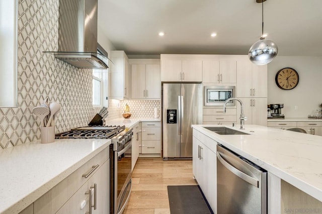 kitchen featuring appliances with stainless steel finishes, hanging light fixtures, light stone countertops, wall chimney exhaust hood, and sink