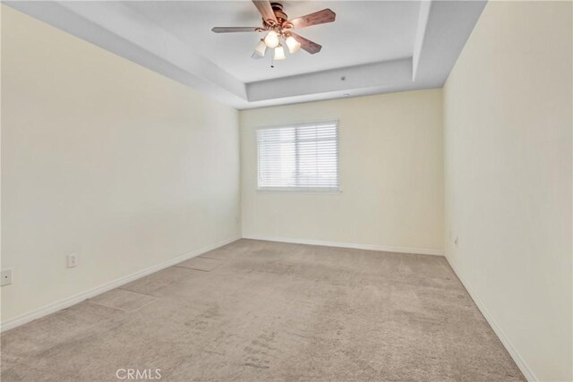 empty room featuring ceiling fan, light carpet, and a raised ceiling