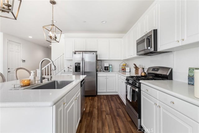 kitchen with an island with sink, appliances with stainless steel finishes, hanging light fixtures, white cabinets, and sink