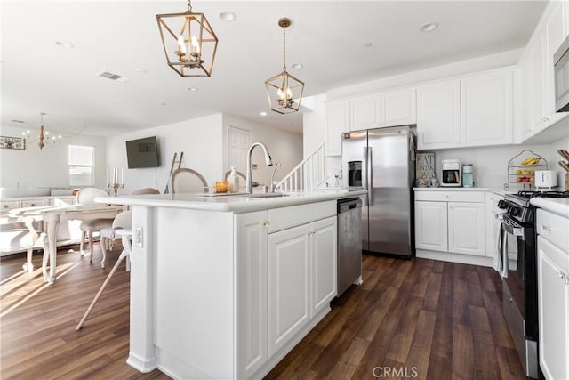 kitchen featuring appliances with stainless steel finishes, white cabinets, hanging light fixtures, and a kitchen island with sink