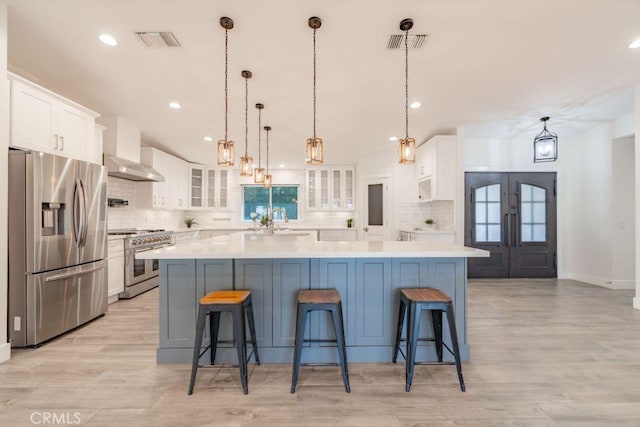 kitchen with appliances with stainless steel finishes, white cabinetry, a kitchen breakfast bar, hanging light fixtures, and a large island