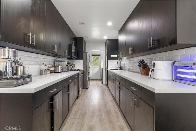 kitchen featuring appliances with stainless steel finishes, light hardwood / wood-style flooring, tasteful backsplash, and sink