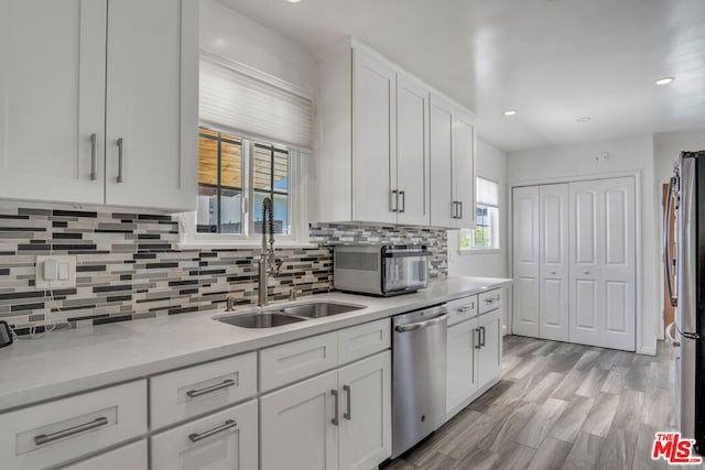 kitchen with backsplash, sink, white cabinetry, stainless steel appliances, and light stone counters