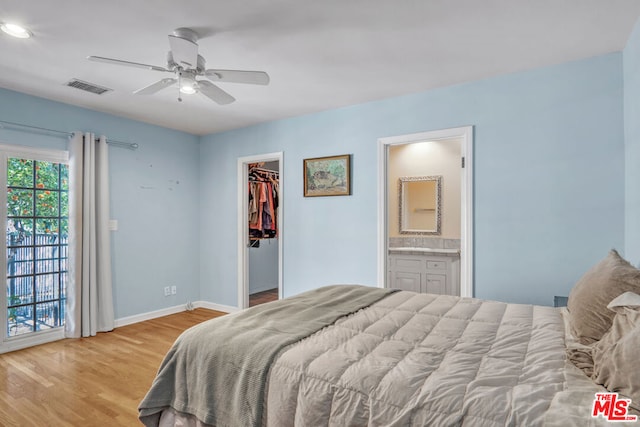 bedroom featuring a walk in closet, a closet, light wood-type flooring, ceiling fan, and ensuite bathroom