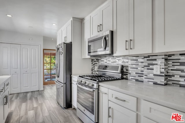 kitchen with light hardwood / wood-style floors, stainless steel appliances, decorative backsplash, light stone countertops, and white cabinets