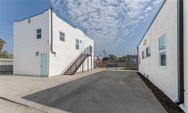 view of side of property featuring a patio area, fence, stairway, and stucco siding