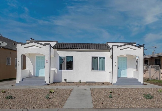 mediterranean / spanish house featuring stucco siding, a tiled roof, and fence