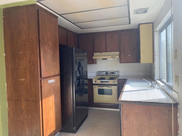 kitchen featuring light tile patterned floors, tile counters, black fridge, white electric range, and sink