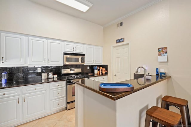 kitchen featuring a breakfast bar, white cabinetry, appliances with stainless steel finishes, kitchen peninsula, and backsplash