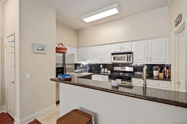 kitchen with tasteful backsplash, dark stone countertops, kitchen peninsula, stainless steel appliances, and white cabinets