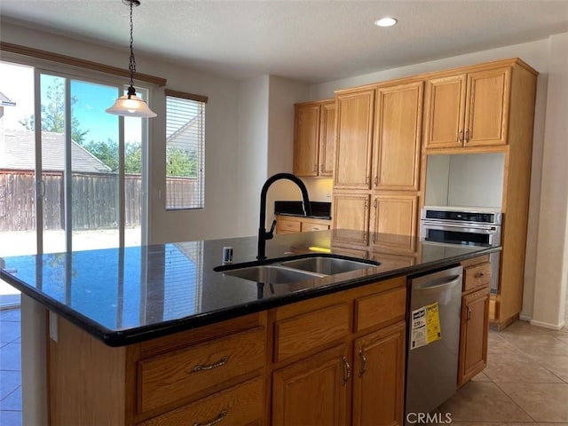 kitchen with light tile patterned floors, an island with sink, appliances with stainless steel finishes, dark stone counters, and sink