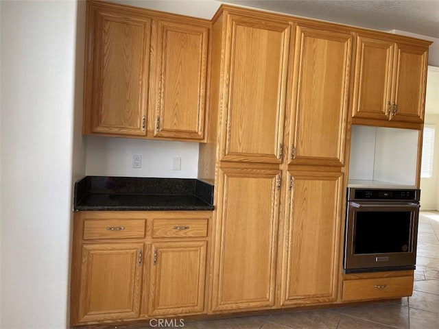 kitchen with dark tile patterned floors, dark stone countertops, and oven