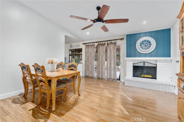 dining room featuring ceiling fan, light wood-type flooring, a fireplace, and lofted ceiling