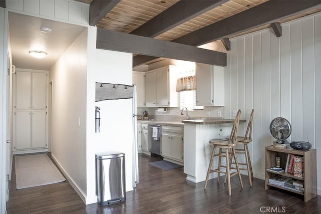 kitchen with appliances with stainless steel finishes, a kitchen bar, white cabinetry, dark hardwood / wood-style floors, and beam ceiling