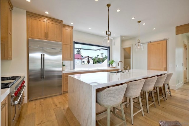 kitchen featuring stainless steel built in fridge, pendant lighting, a kitchen island with sink, and light hardwood / wood-style flooring