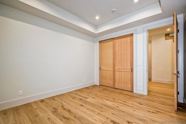 unfurnished bedroom with hardwood / wood-style flooring, a tray ceiling, and a closet