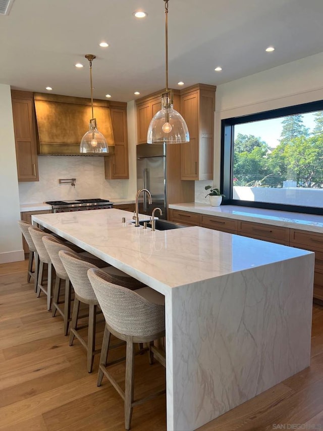 kitchen with built in refrigerator, a large island, light stone countertops, and decorative light fixtures