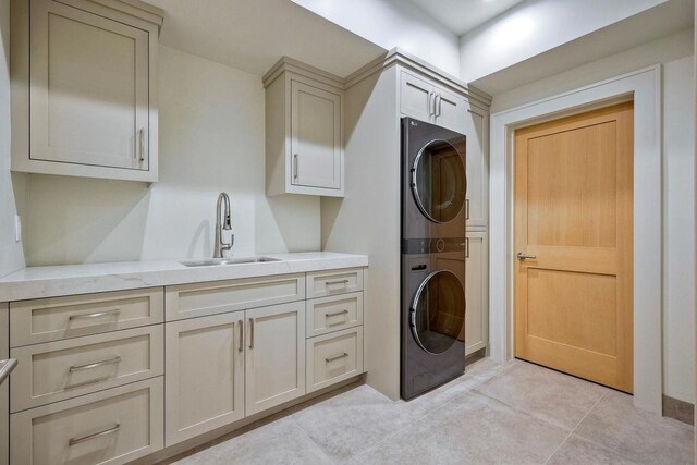 laundry area with cabinets, stacked washer / drying machine, sink, and light tile patterned floors