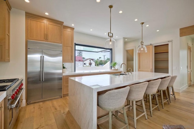 kitchen featuring pendant lighting, stainless steel built in refrigerator, an island with sink, sink, and light hardwood / wood-style floors