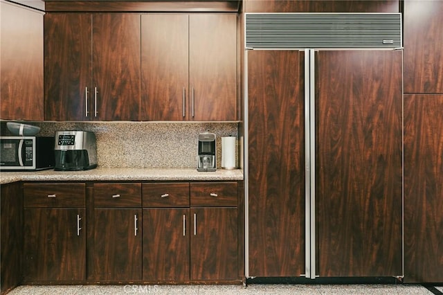 kitchen with tasteful backsplash, dark brown cabinets, and paneled built in fridge