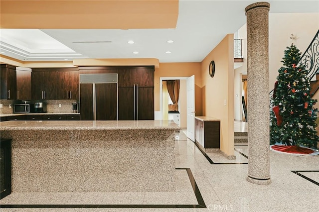 kitchen with paneled built in refrigerator, backsplash, dark brown cabinetry, and decorative columns